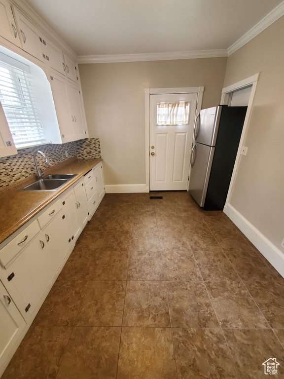 Kitchen featuring a sink, freestanding refrigerator, ornamental molding, white cabinetry, and tasteful backsplash