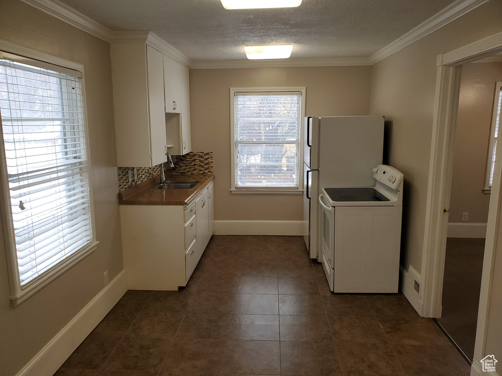 Kitchen with washer / dryer, a sink, white cabinetry, baseboards, and ornamental molding