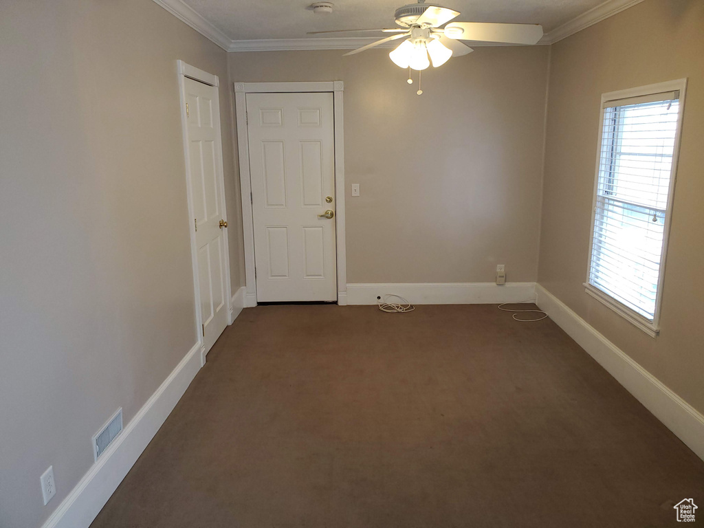 Unfurnished room featuring dark carpet, crown molding, ceiling fan, plenty of natural light, and baseboards