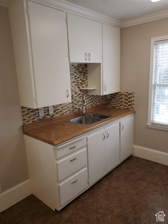 Kitchen with a sink, decorative backsplash, baseboards, white cabinetry, and ornamental molding