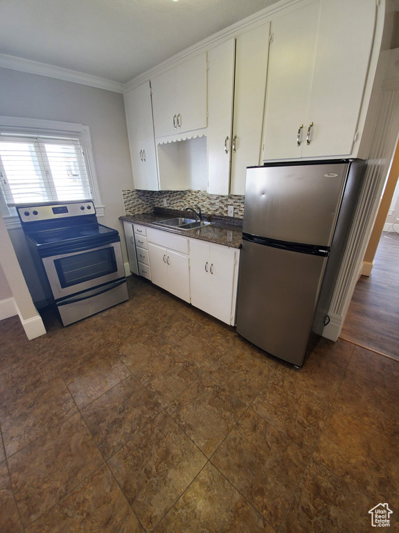 Kitchen with stainless steel appliances, a sink, crown molding, dark countertops, and white cabinetry