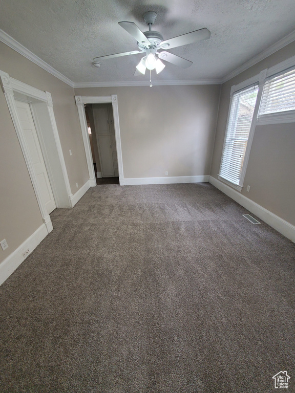 Carpeted spare room featuring a textured ceiling, a ceiling fan, crown molding, and baseboards