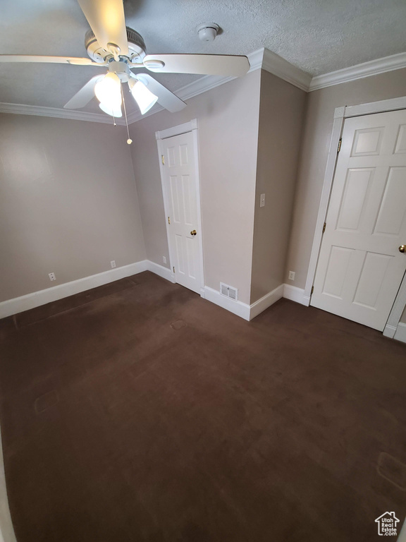 Unfurnished bedroom featuring baseboards, dark carpet, ornamental molding, and ceiling fan