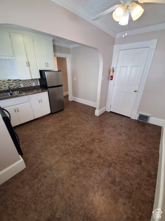Kitchen with a sink, freestanding refrigerator, dark countertops, ornamental molding, and ceiling fan