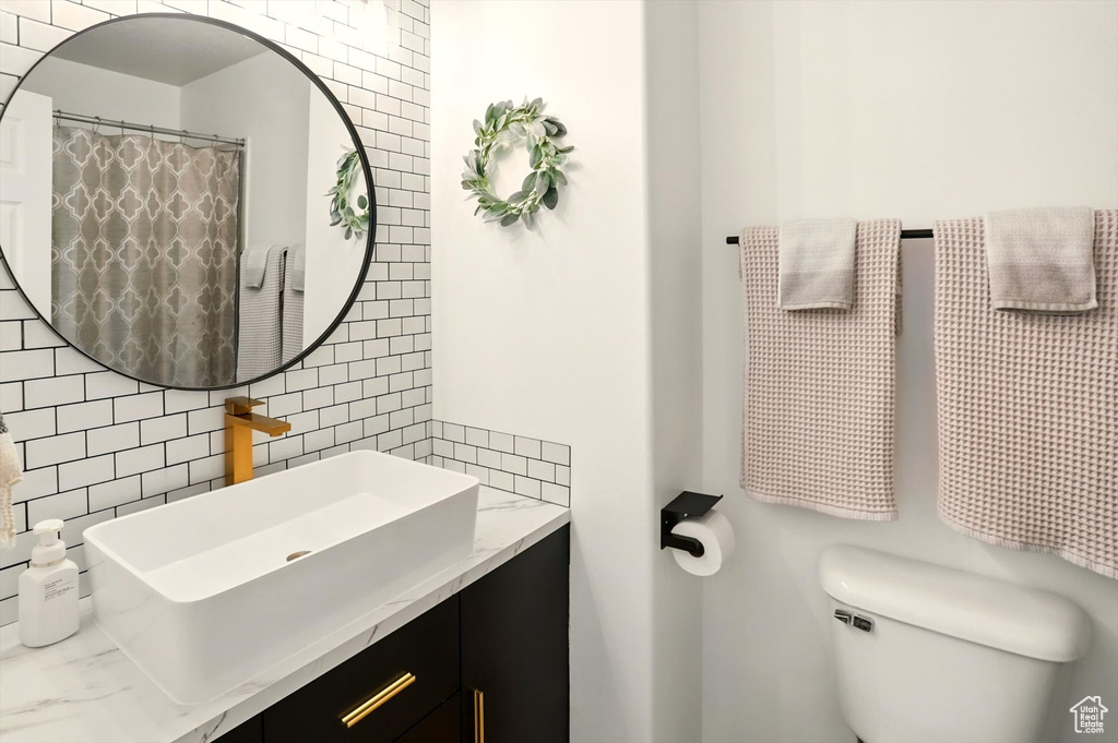 Bathroom with tile walls, toilet, vanity, and decorative backsplash