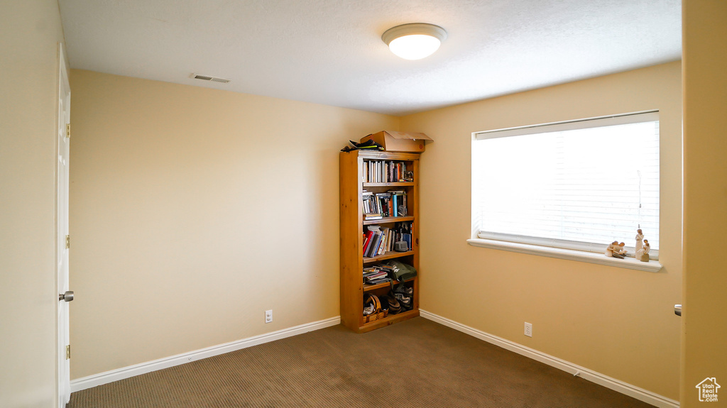 Spare room featuring dark colored carpet and baseboards