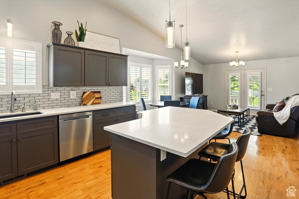 Kitchen featuring stainless steel dishwasher, vaulted ceiling, open floor plan, a sink, and a chandelier