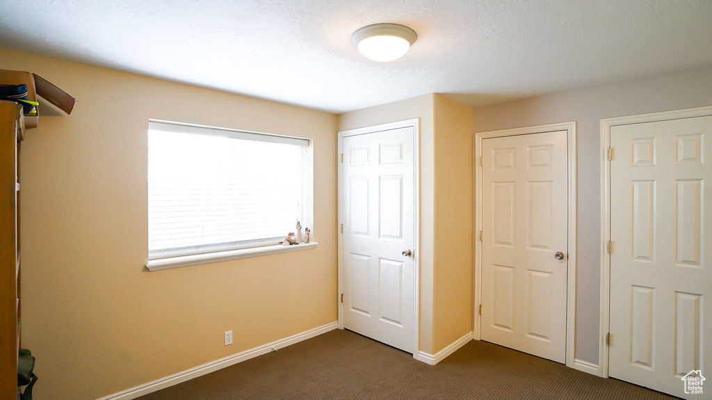 Unfurnished bedroom with dark colored carpet and baseboards