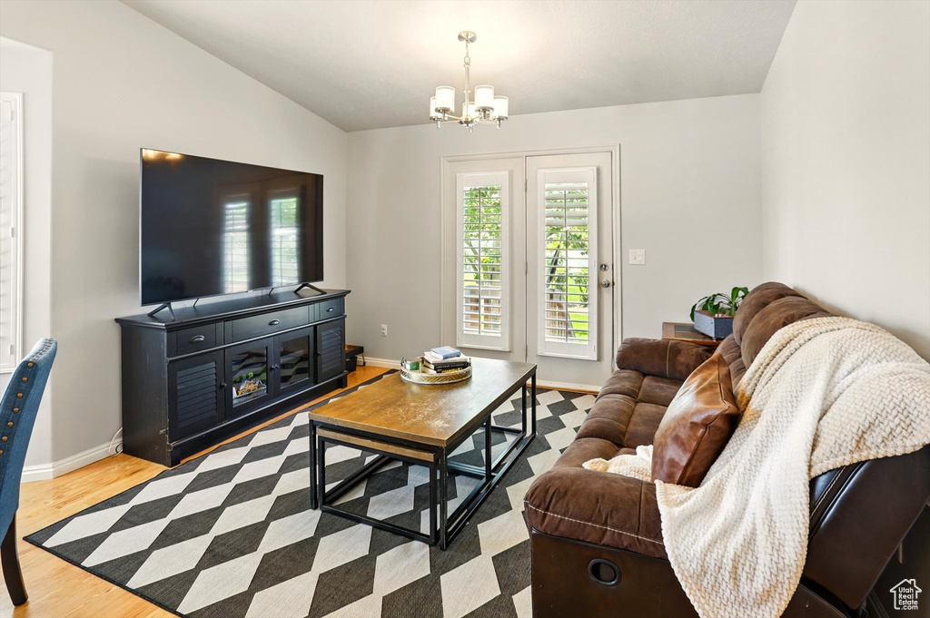Living room with vaulted ceiling, a chandelier, wood finished floors, and baseboards