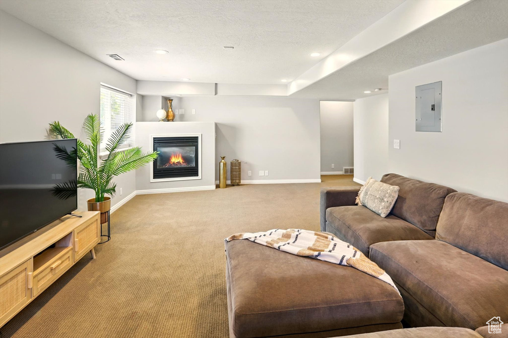 Carpeted living room with electric panel, baseboards, a glass covered fireplace, and recessed lighting