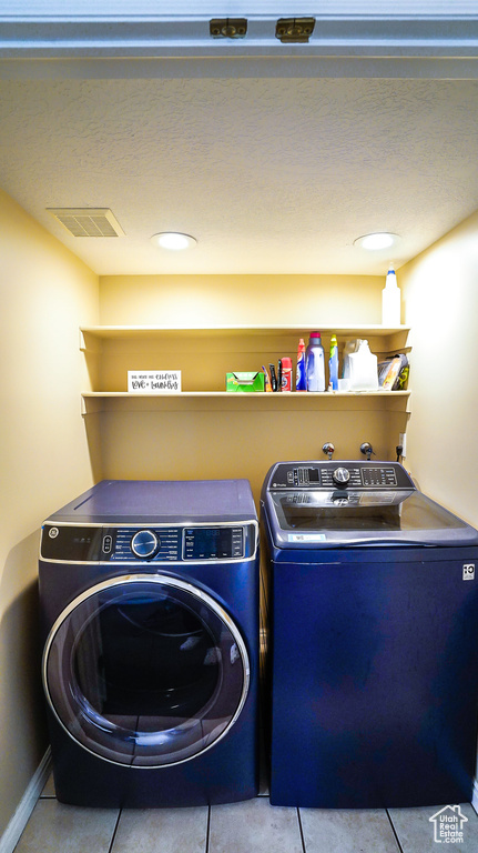Washroom with washing machine and dryer and tile patterned flooring
