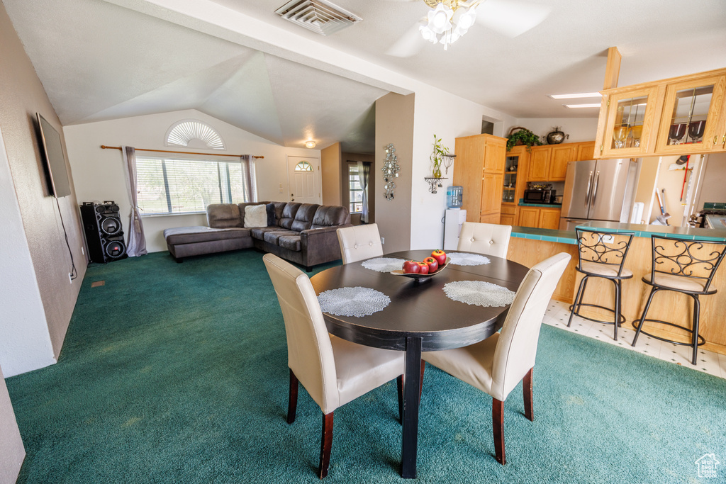 Dining area with light carpet, ceiling fan, and vaulted ceiling