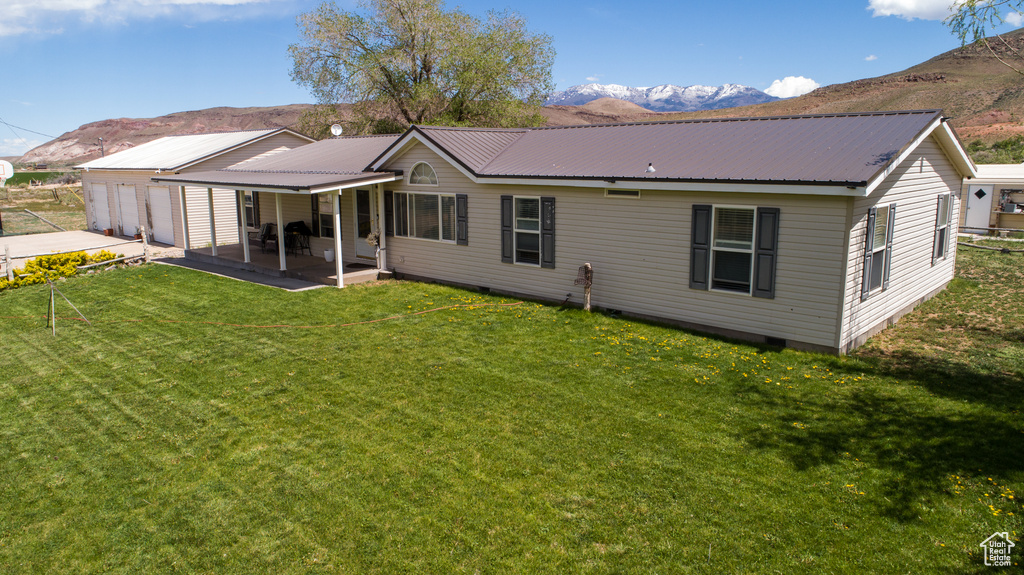 Back of house featuring a mountain view, a lawn, a garage, and metal roof