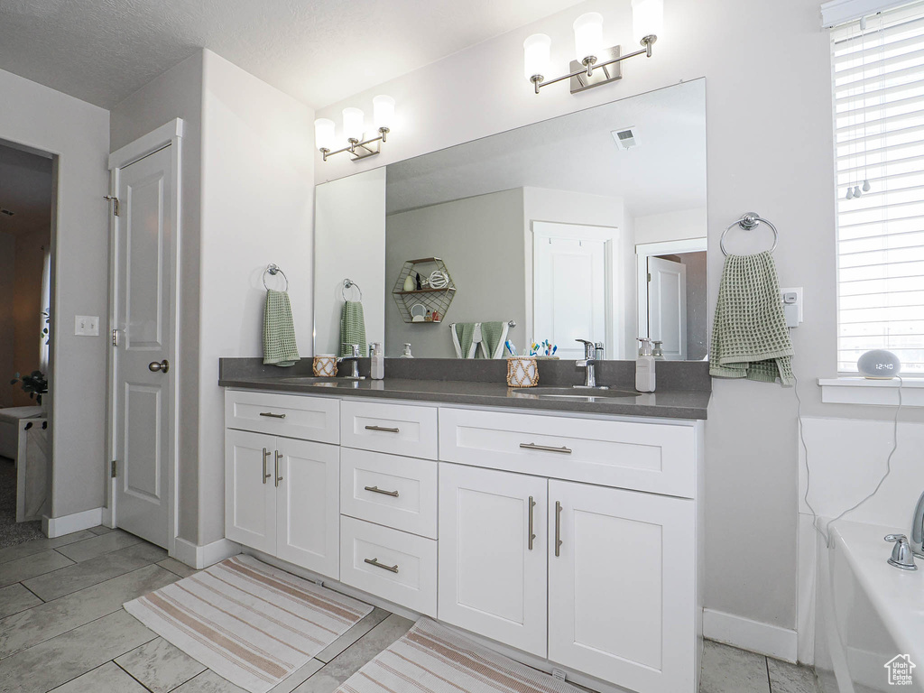Full bathroom featuring double vanity, baseboards, and a bath