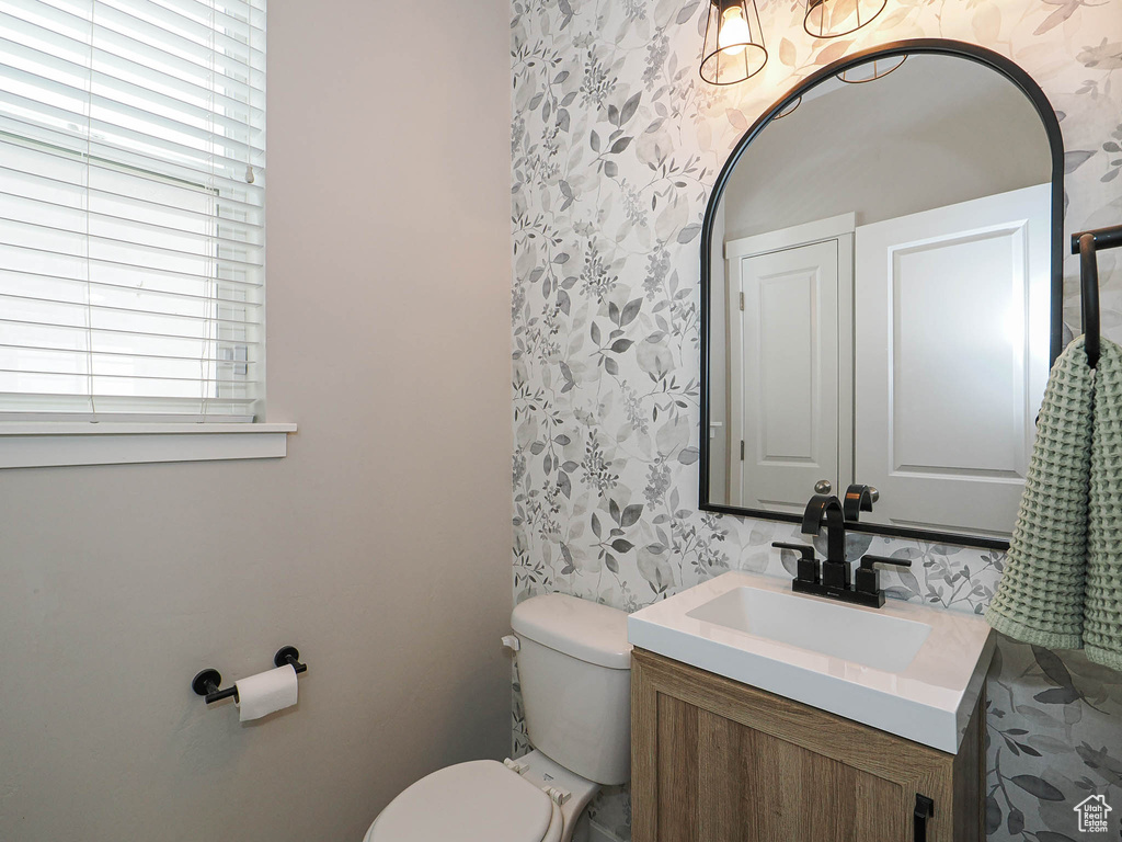 Half bathroom featuring wallpapered walls, vanity, and toilet