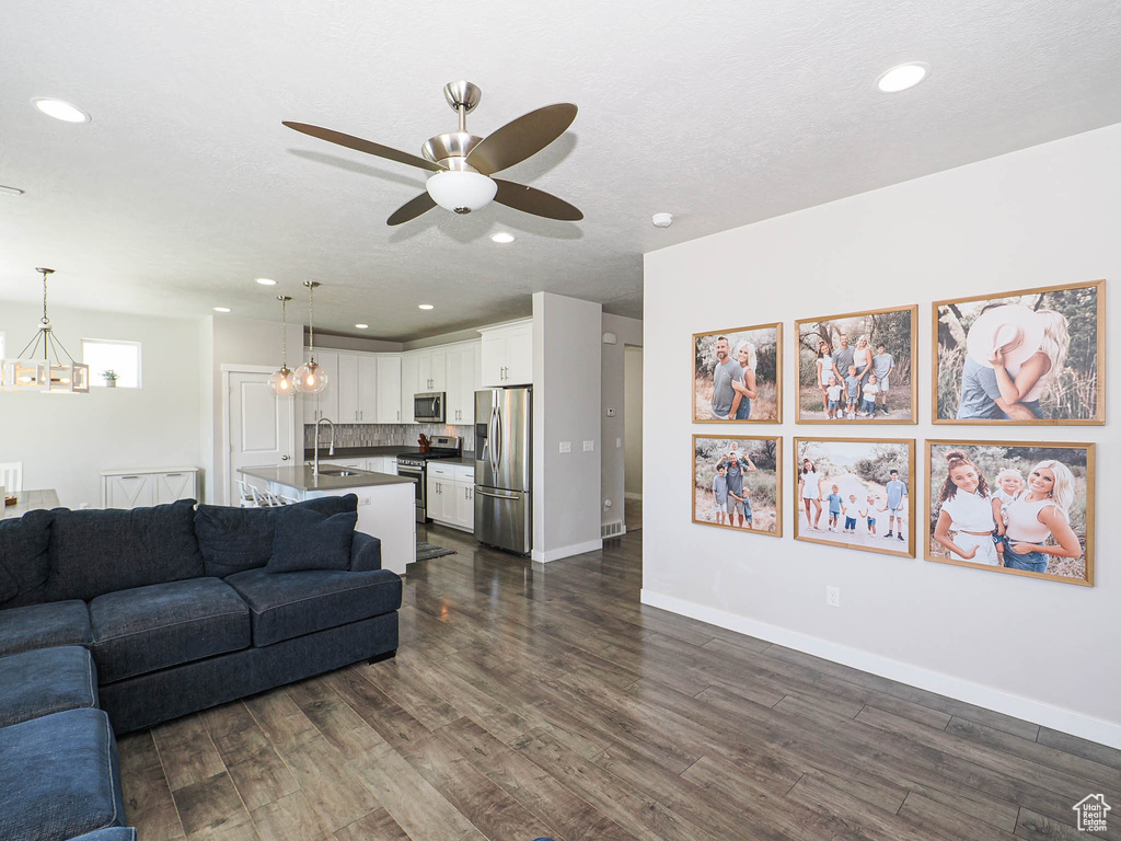 Living room with a chandelier, dark wood-type flooring, ceiling fan, recessed lighting, and baseboards