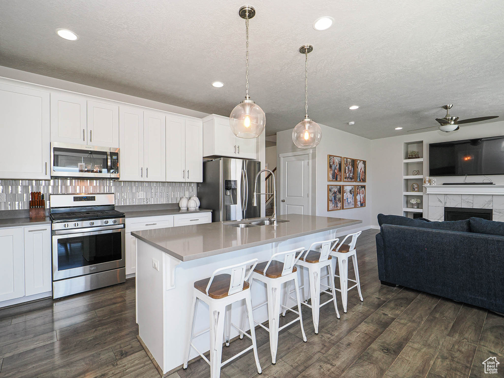 Kitchen featuring appliances with stainless steel finishes, open floor plan, a textured ceiling, dark wood-style flooring, and a sink