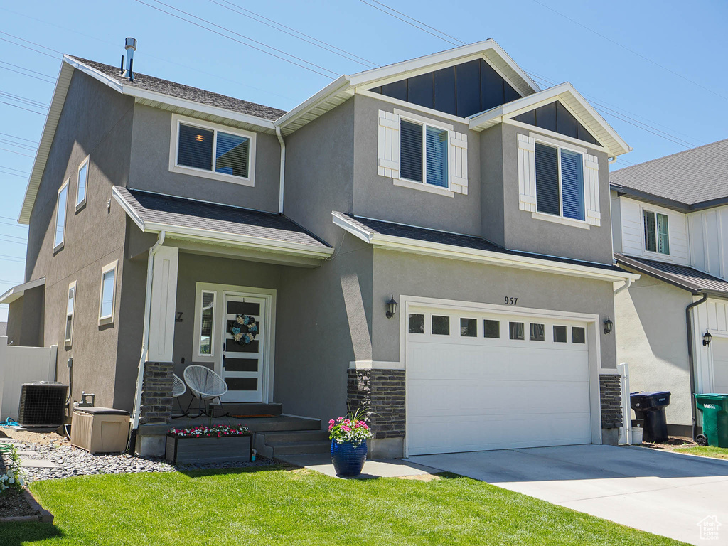 View of front of home with stucco siding, an attached garage, cooling unit, a front yard, and concrete driveway