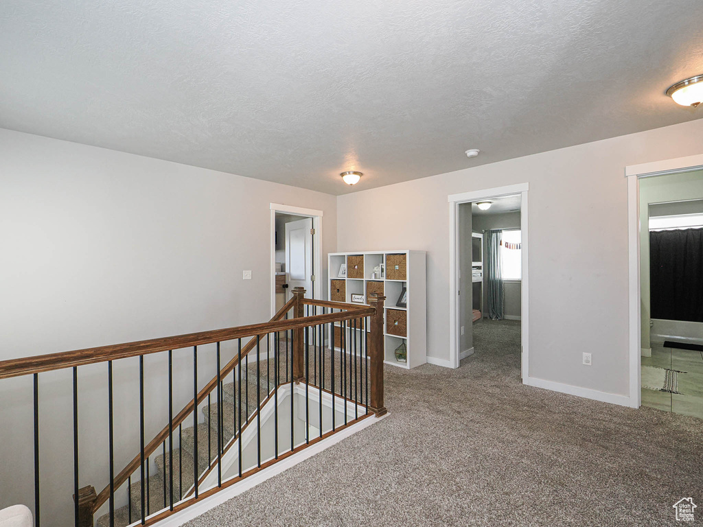 Corridor featuring an upstairs landing, carpet flooring, baseboards, and a textured ceiling