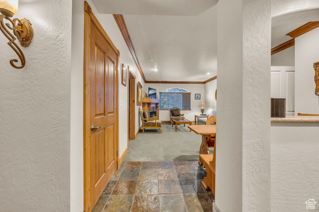Corridor featuring a textured wall, crown molding, dark stone finish floors, baseboards, and dark colored carpet