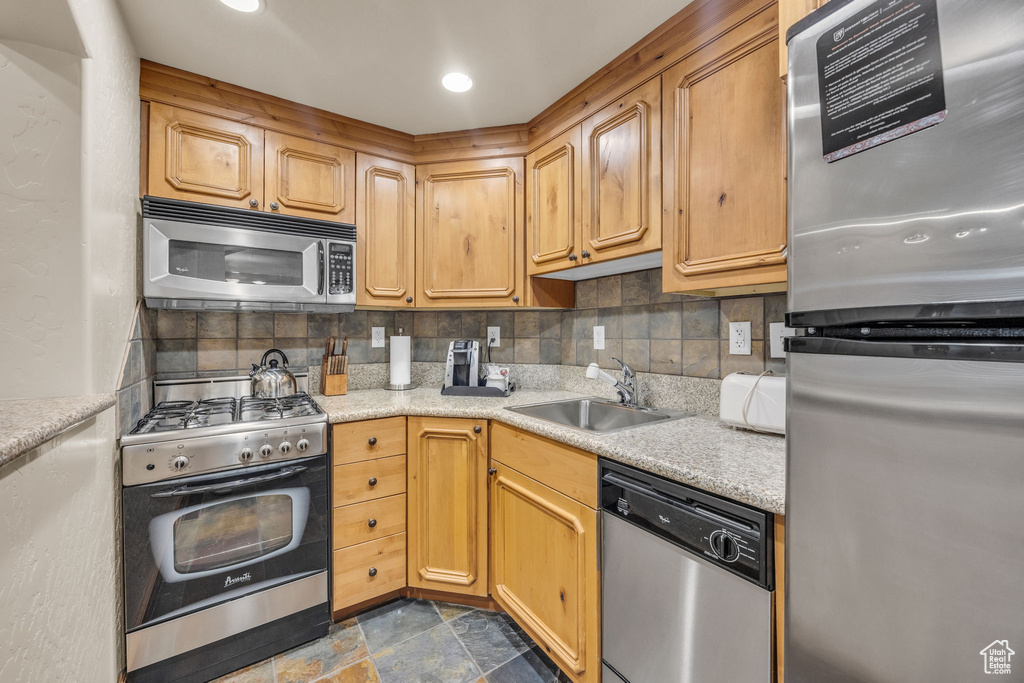 Kitchen featuring appliances with stainless steel finishes, decorative backsplash, a sink, and dark stone finish floors