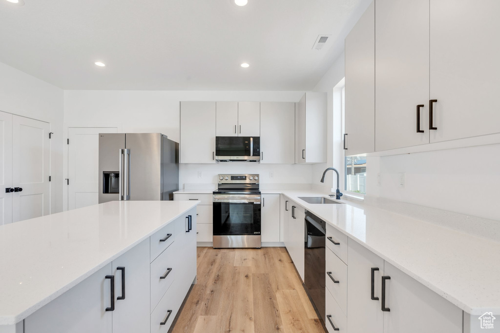 Kitchen with appliances with stainless steel finishes, a sink, light wood finished floors, recessed lighting, and a center island