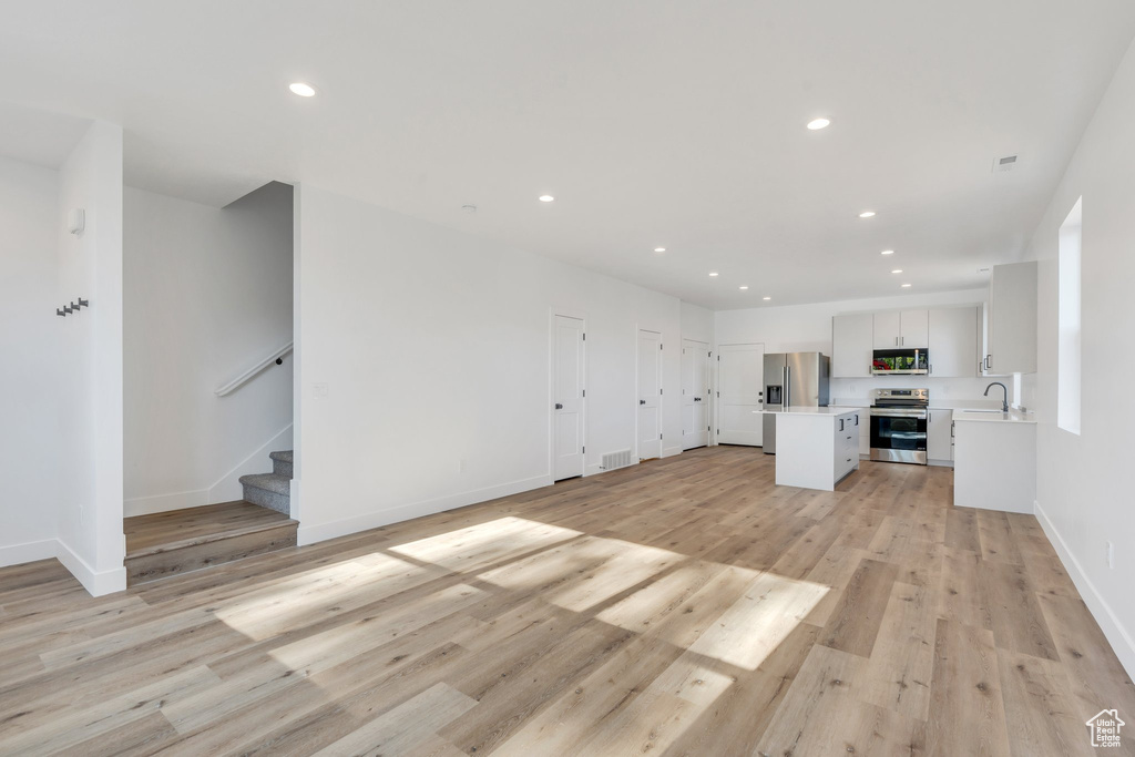 Unfurnished living room featuring recessed lighting, stairs, baseboards, light wood-type flooring, and a sink