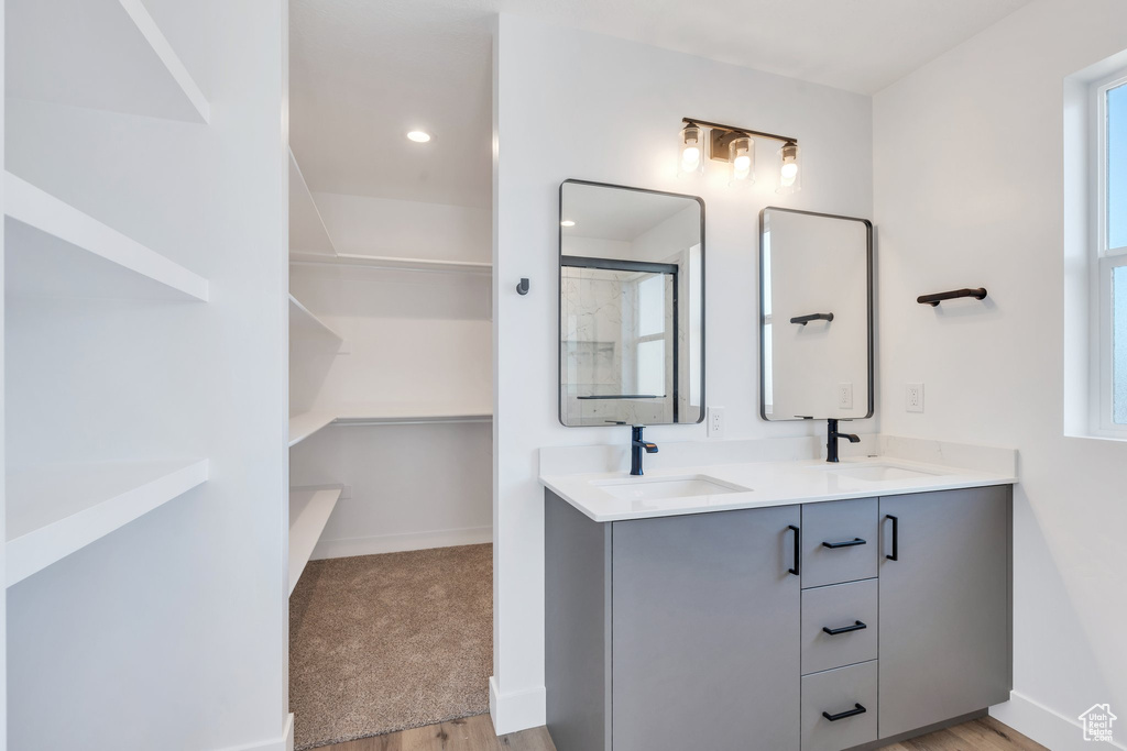 Full bathroom with double vanity, wood finished floors, baseboards, a spacious closet, and recessed lighting