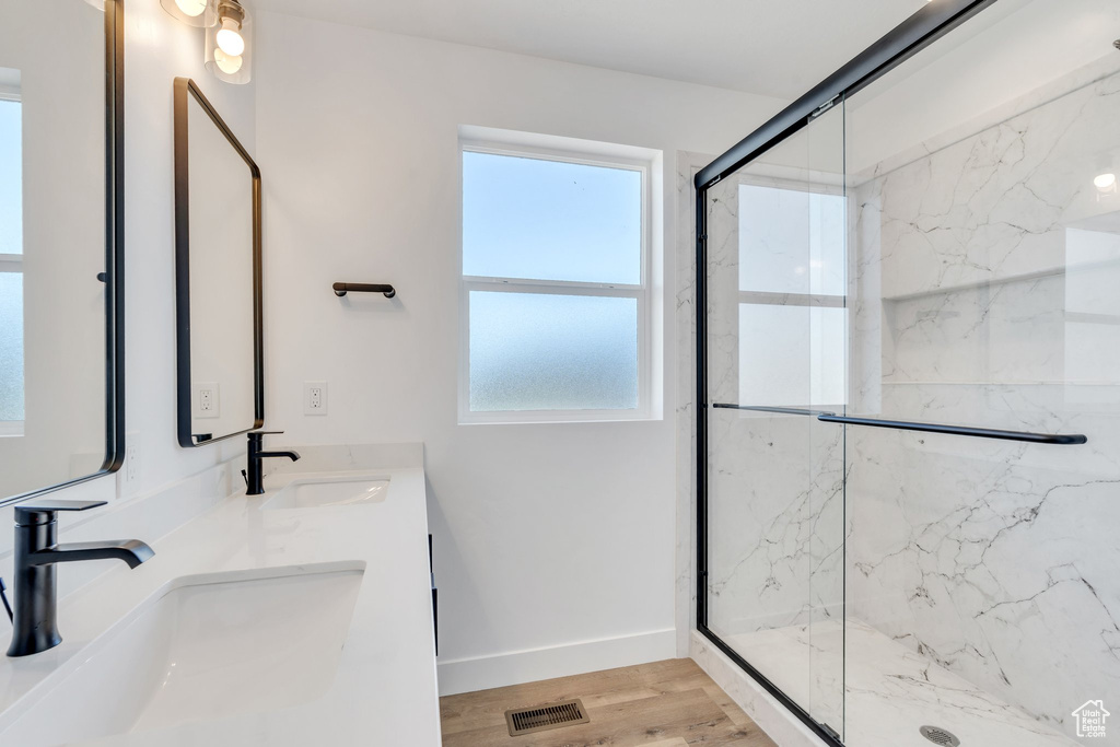 Full bath with a marble finish shower, double vanity, wood finished floors, and baseboards