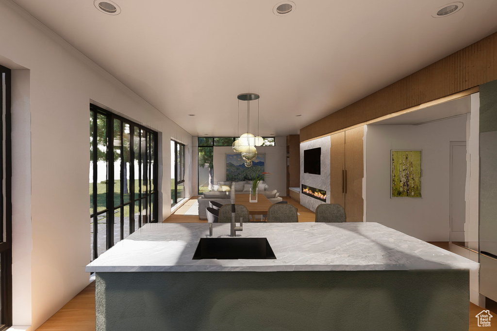 Kitchen with a sink, a lit fireplace, decorative light fixtures, light wood-style floors, and a center island with sink