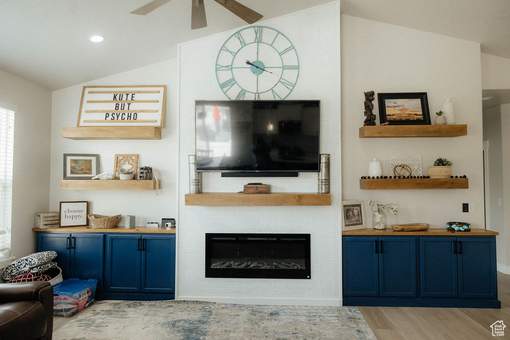 Living area with vaulted ceiling, wood finished floors, ceiling fan, and a large fireplace