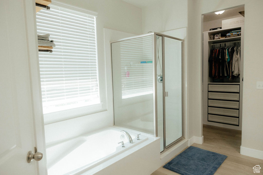Bathroom with a shower stall, a garden tub, a spacious closet, wood finished floors, and baseboards