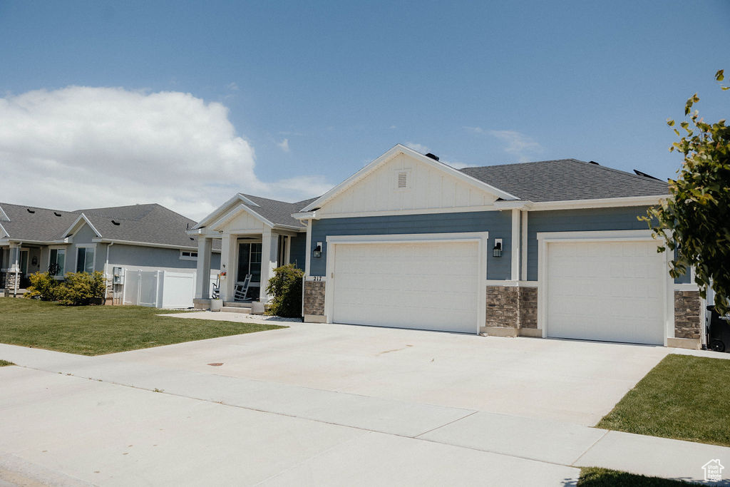 View of front of property featuring a garage, driveway, a front lawn, board and batten siding, and stone siding