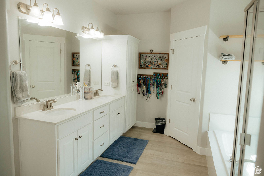 Full bath featuring wood finished floors, double vanity, a shower, a bathtub, and baseboards
