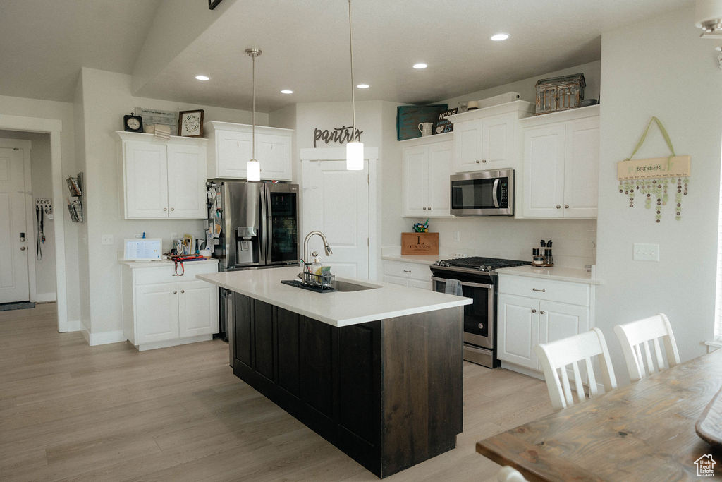 Kitchen with appliances with stainless steel finishes, a sink, white cabinets, light countertops, and recessed lighting
