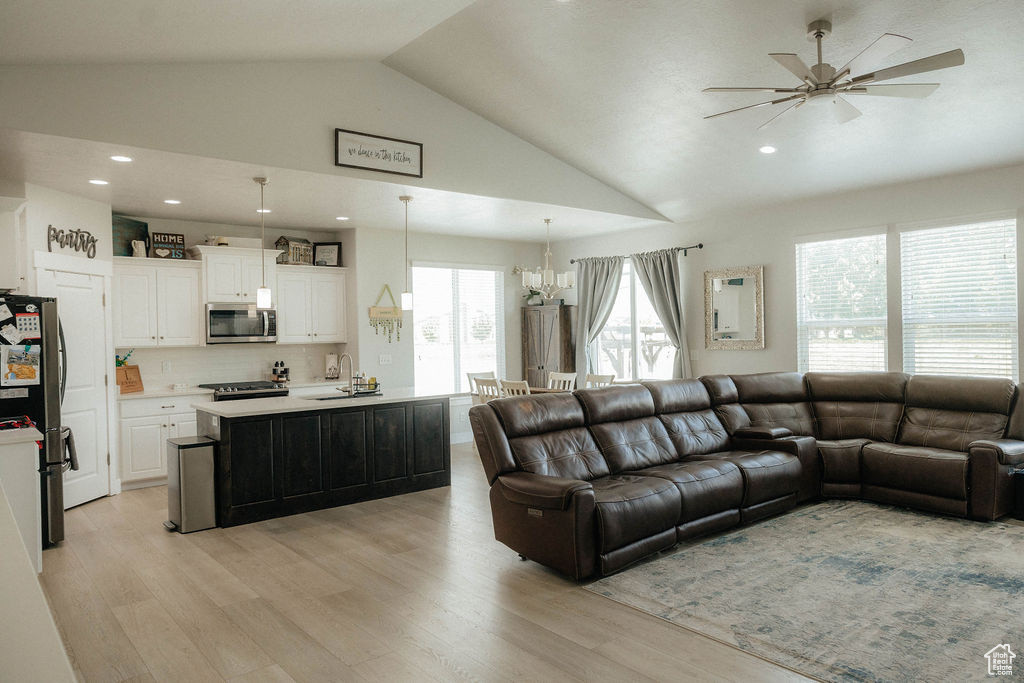 Living room featuring vaulted ceiling, ceiling fan, a chandelier, light wood-style flooring, and recessed lighting
