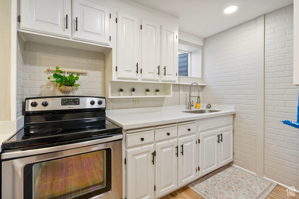 Kitchen featuring stainless steel electric range oven, a sink, light countertops, white cabinets, and brick wall