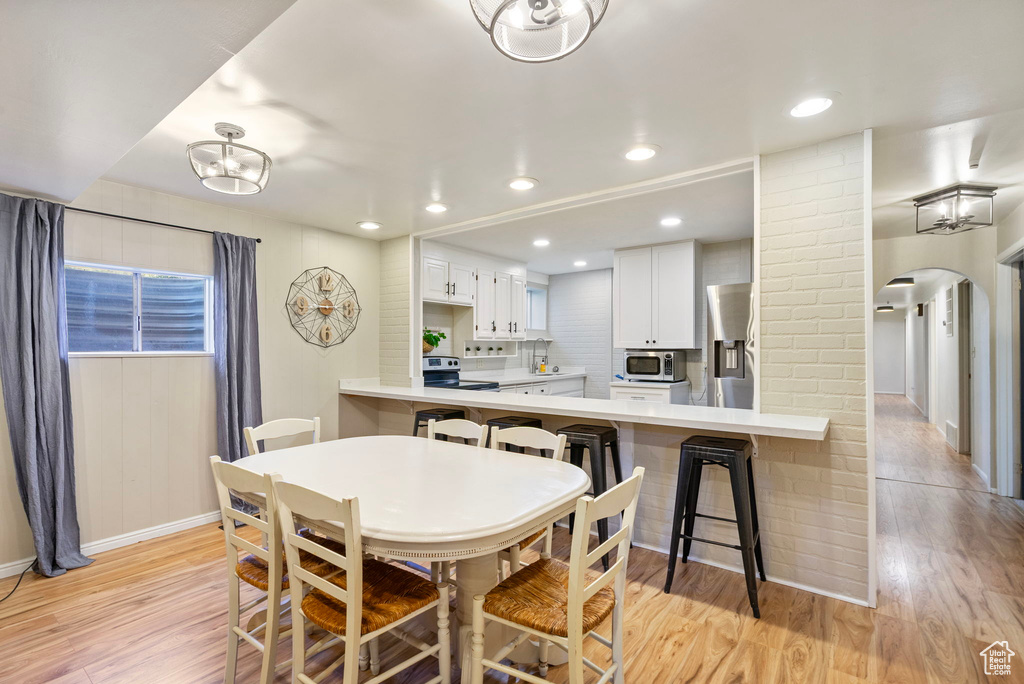 Dining space with arched walkways, light wood-style flooring, baseboards, and recessed lighting
