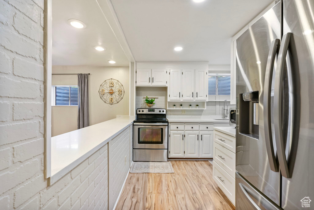 Kitchen with stainless steel appliances, light wood finished floors, light countertops, white cabinetry, and recessed lighting