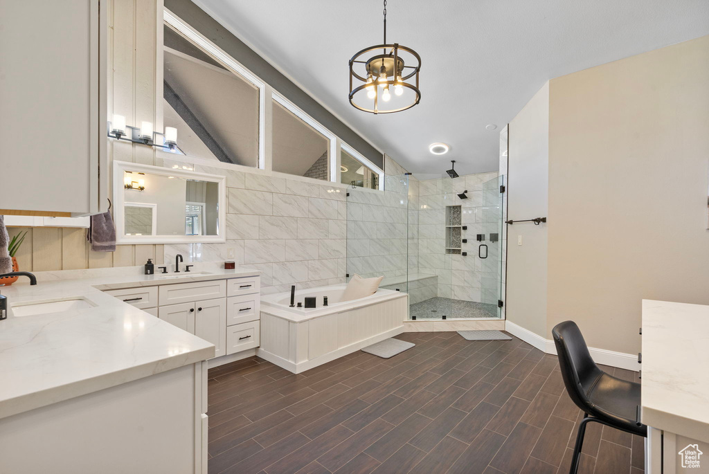 Full bathroom with lofted ceiling, a chandelier, a shower stall, double vanity, and a garden tub