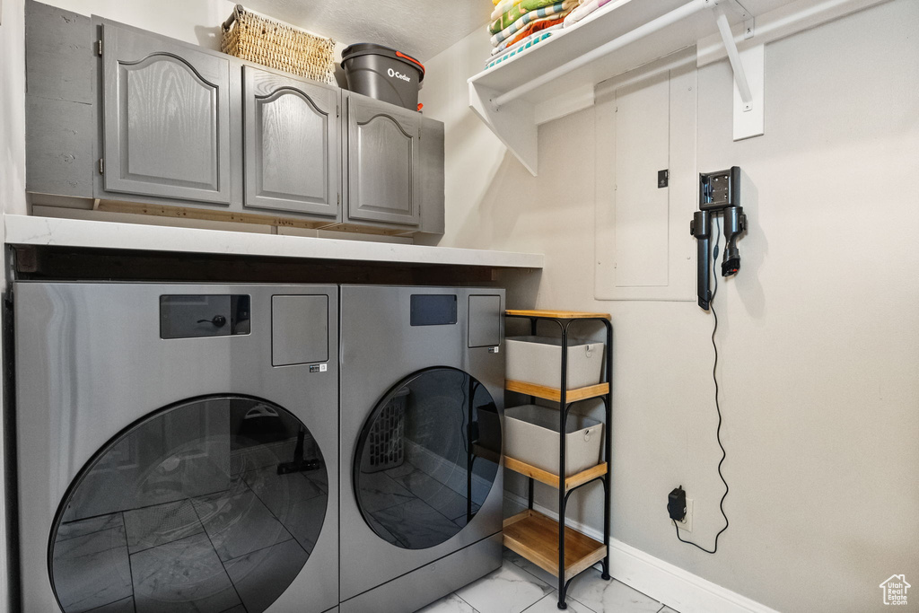 Laundry area featuring cabinet space, light marble finish flooring, washing machine and clothes dryer, and baseboards