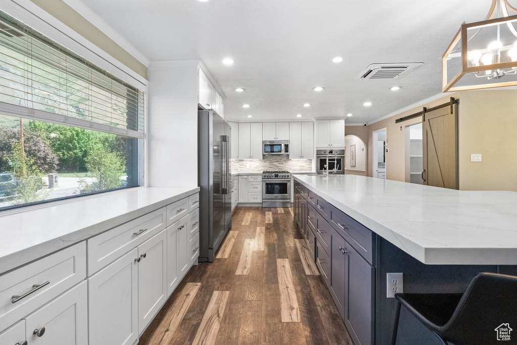 Kitchen featuring high end appliances, a barn door, white cabinets, ornamental molding, and recessed lighting