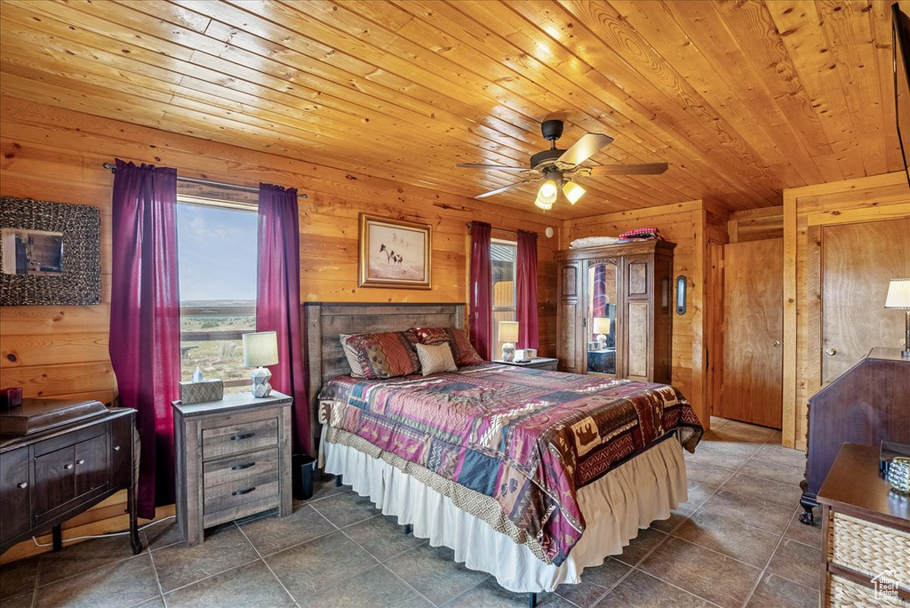 Bedroom with wooden walls, wooden ceiling, dark tile patterned flooring, and a ceiling fan