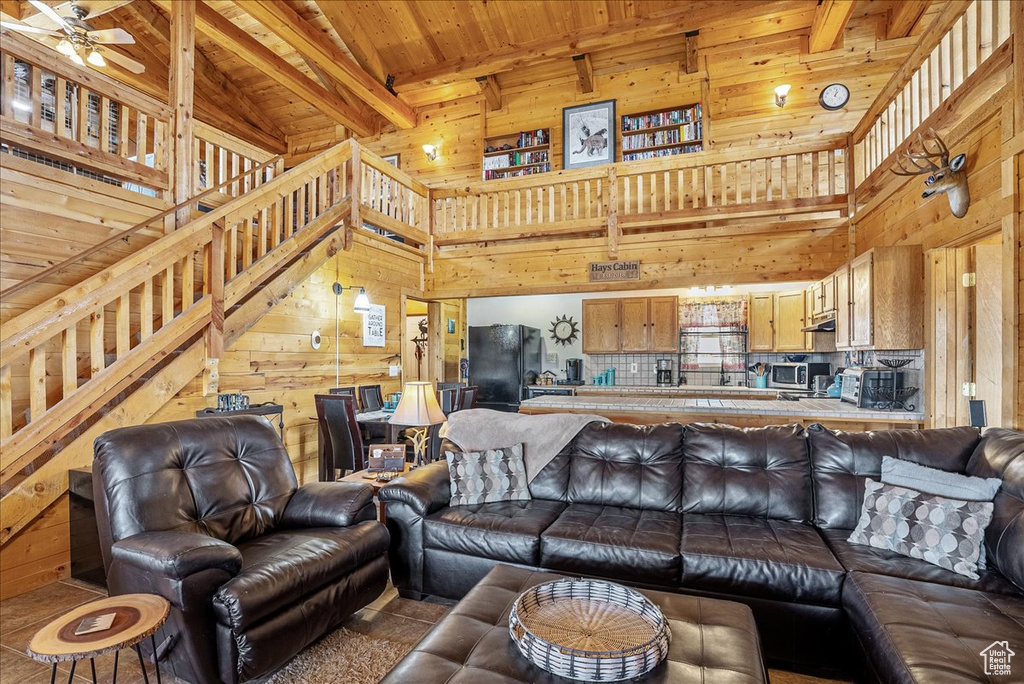 Living area with wooden walls, wooden ceiling, a towering ceiling, beamed ceiling, and a ceiling fan