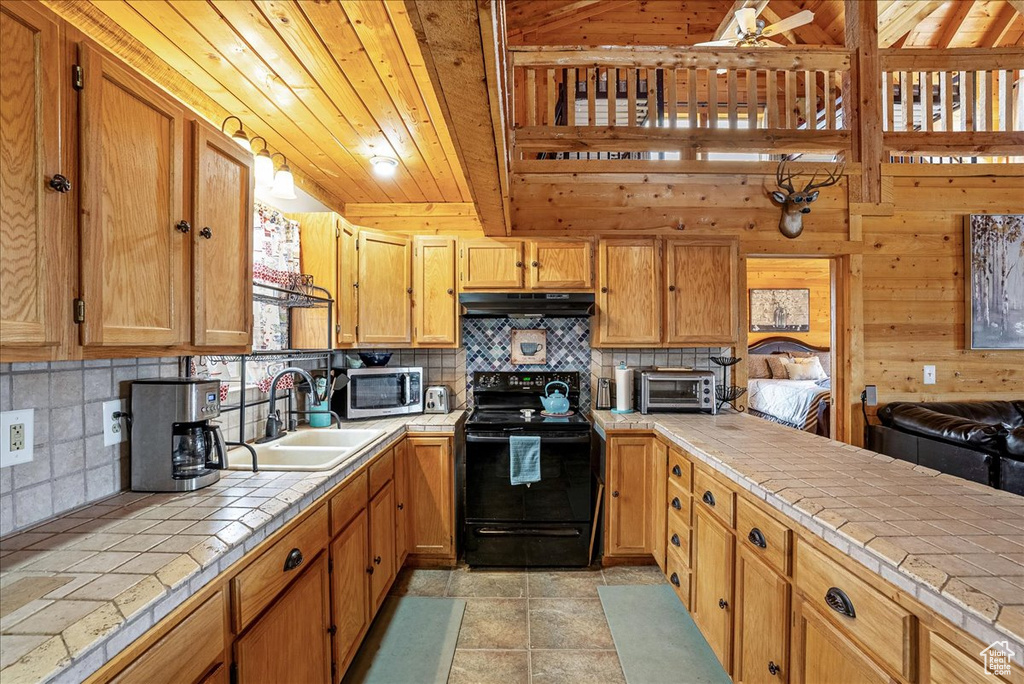 Kitchen featuring tile counters, black electric range oven, a sink, stainless steel microwave, and under cabinet range hood