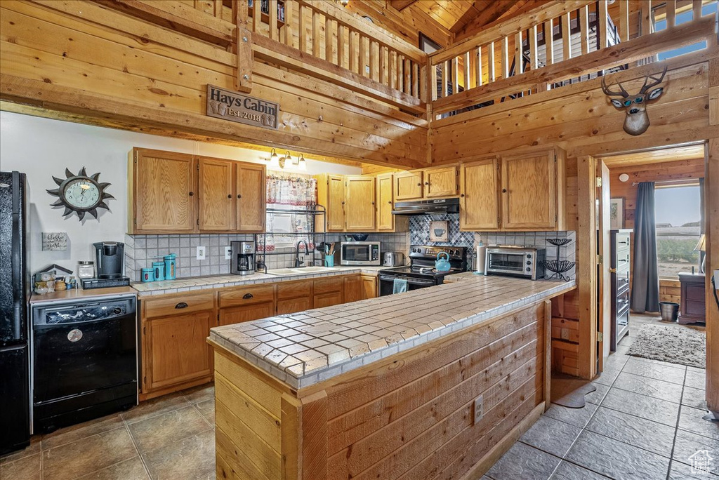 Kitchen with range with electric stovetop, tile counters, black dishwasher, under cabinet range hood, and tasteful backsplash