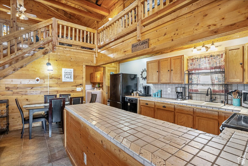 Kitchen with tile countertops, freestanding refrigerator, a sink, tasteful backsplash, and wood walls