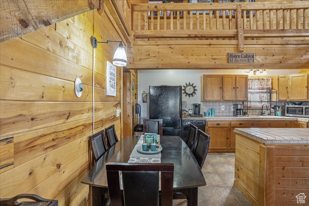 Kitchen featuring tile counters, stainless steel microwave, a sink, wood walls, and decorative backsplash