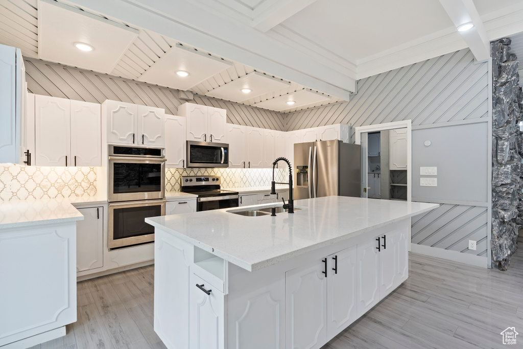 Kitchen with stainless steel appliances, a sink, tasteful backsplash, light countertops, and beamed ceiling
