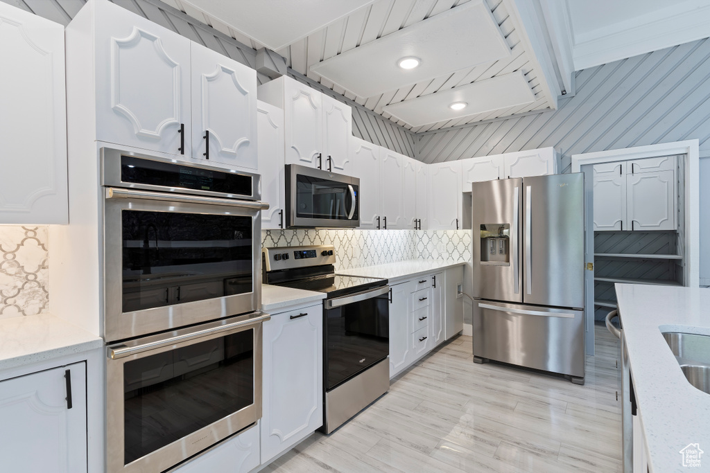Kitchen featuring appliances with stainless steel finishes, backsplash, and white cabinetry